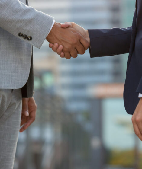 Businesspeople standing in city street and shaking hands. Business man and woman in office suits meeting outside. Successful partnership concept